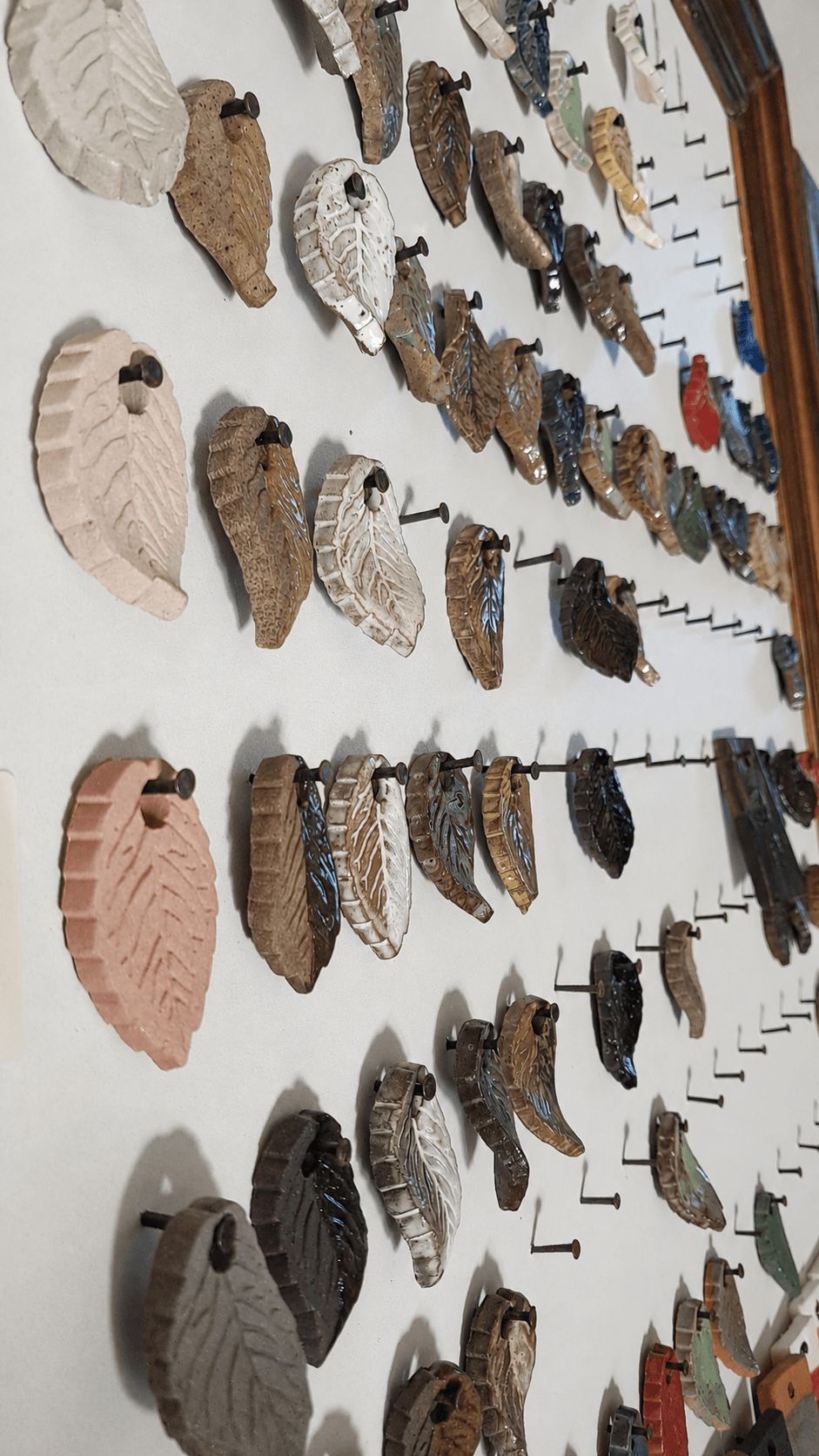 Peças cerâmicas em formato de folhas penduradas na parede do ateliê
